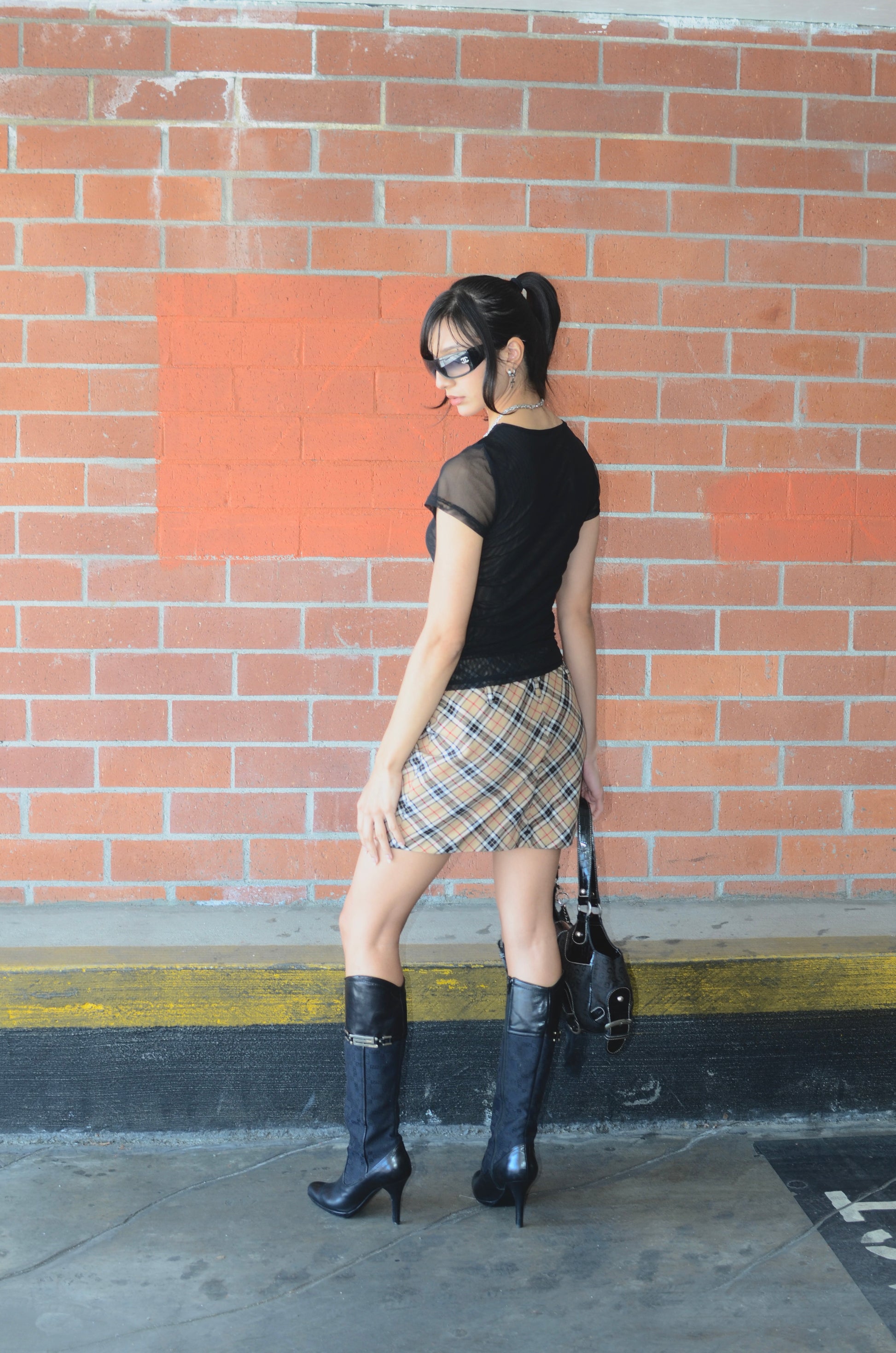 Model wearing black tee, black versace boots, black guess bag, chanel sunglasses, and a vintage Dolce & Gabbana plaid mini skirt displayed on a mannequin, with a side zipper, in a great condition.