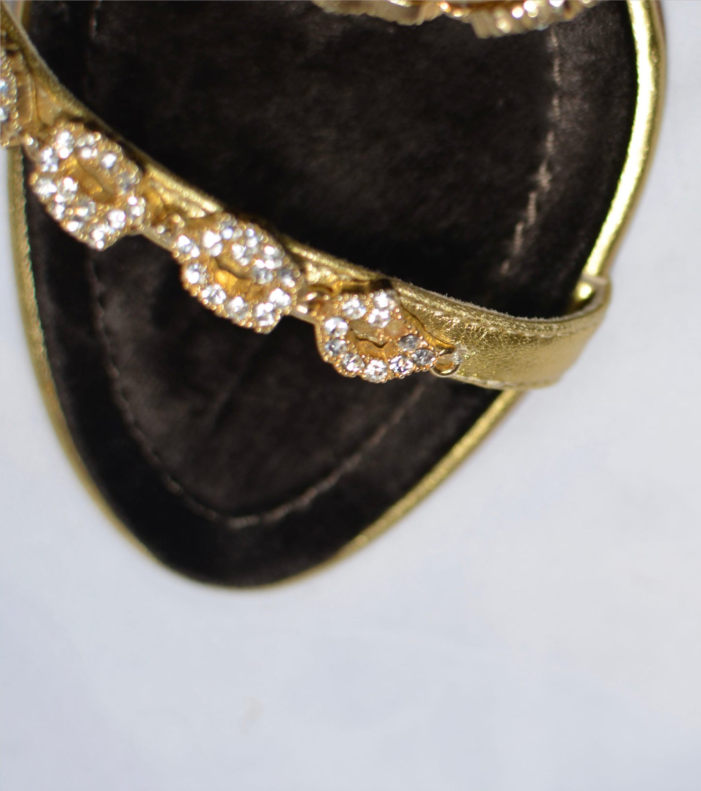 Close up of Gold high-heeled  Giuseppe Zanotti sandals, close up on gold straps with  embellishments and one small crystal missing from strap.